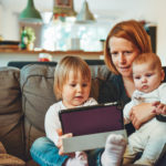 Picture of woman holding two children, reviewing information on a smart device