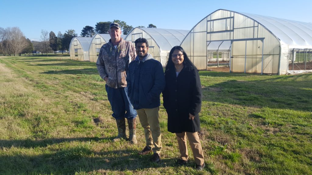 Picture of three people standing in front of greenhouses. 