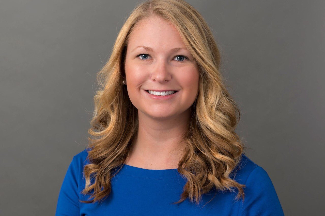 Delaney Foster headshot in blue short sleeved dress in front of a grey background