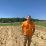 Associate professor Mitchell Richmond stands in front of a field at the Northeast Research and Education Center