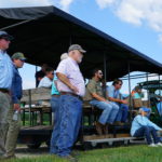Group of producers stand next to wagon while listening to presentation