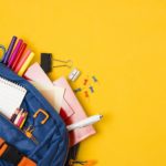 school supplies in a blue backpack with a yellow backdrop