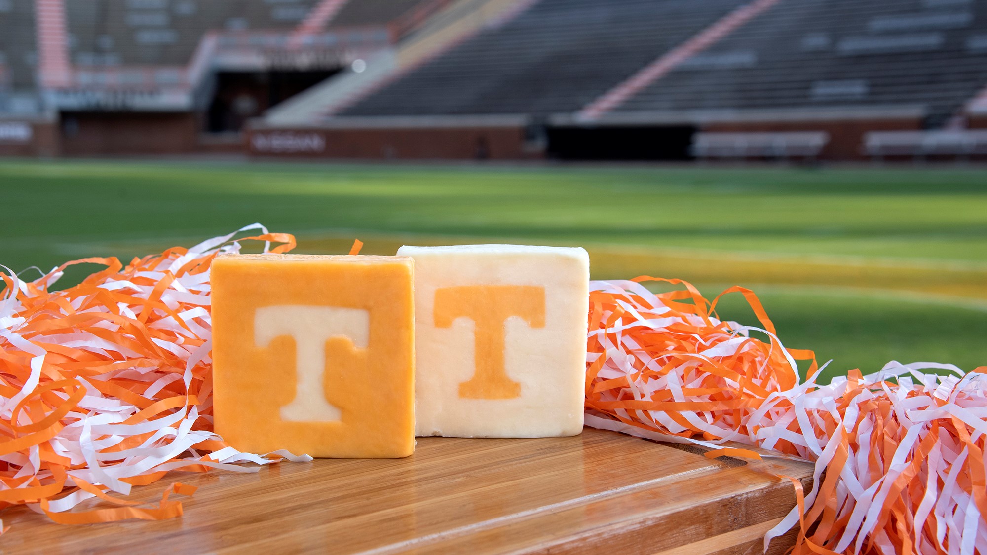 All vol cheese blocks on a table with orange and white streamers surrounding it. Neyland stadium bleachers are in the background