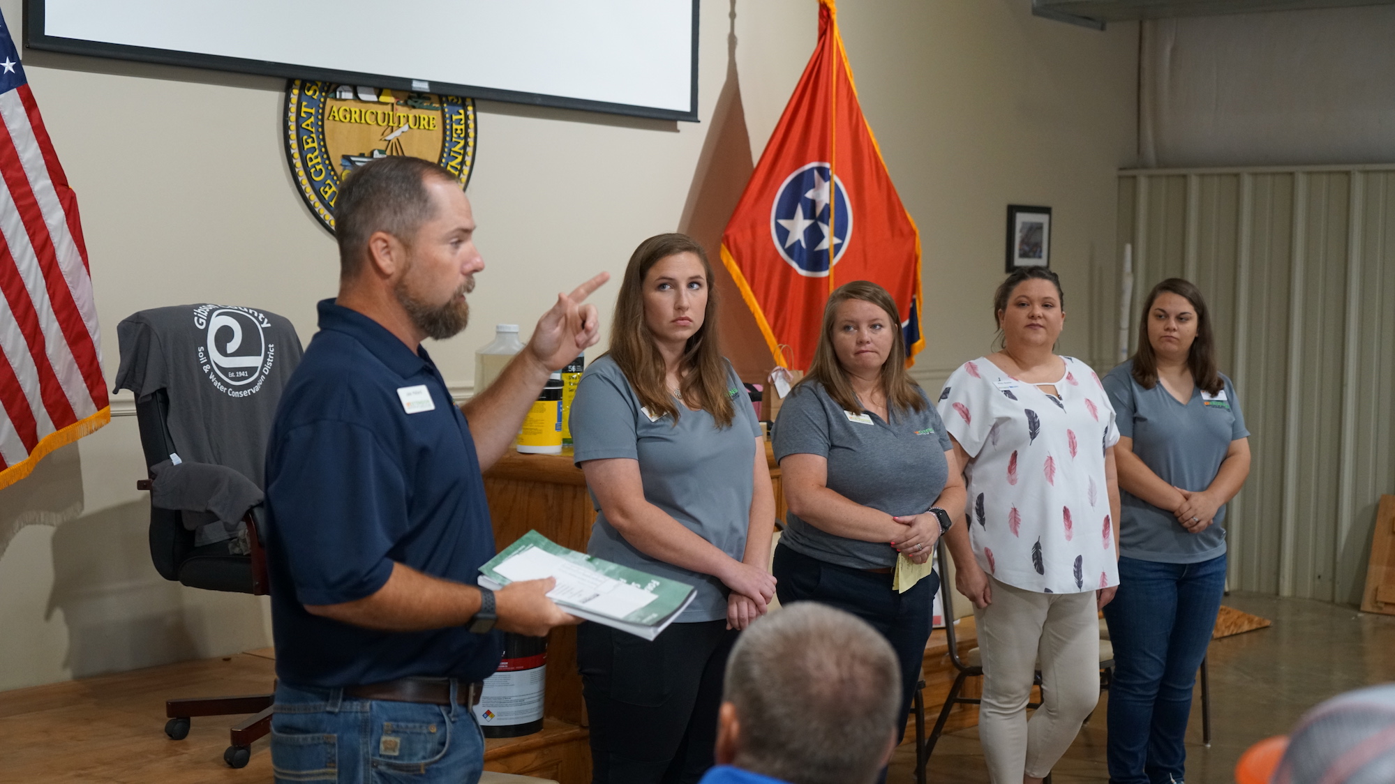 four people stand in front of a Tennessee flag. Left to right are Jake Mallard, Carrie Joyner, Deanna Poole, Misty Brasher and Tori Griffin.