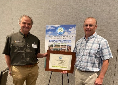 Forbes and Hawkins holding award in front of poster