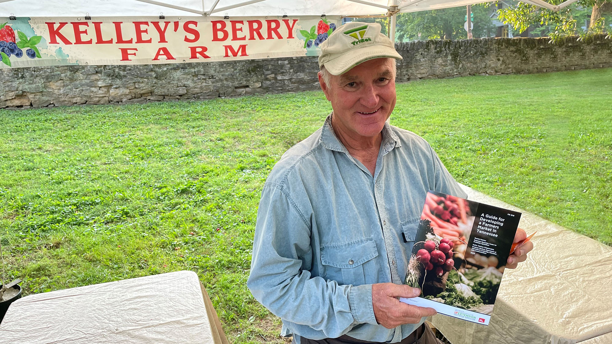 producer at farmers market holding a copy of UT Extension publication, PB 1918 and smiling at camera