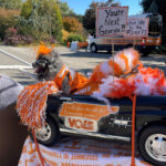 Dog dressed up in UT cheer leading outfit sitting in a miniature car