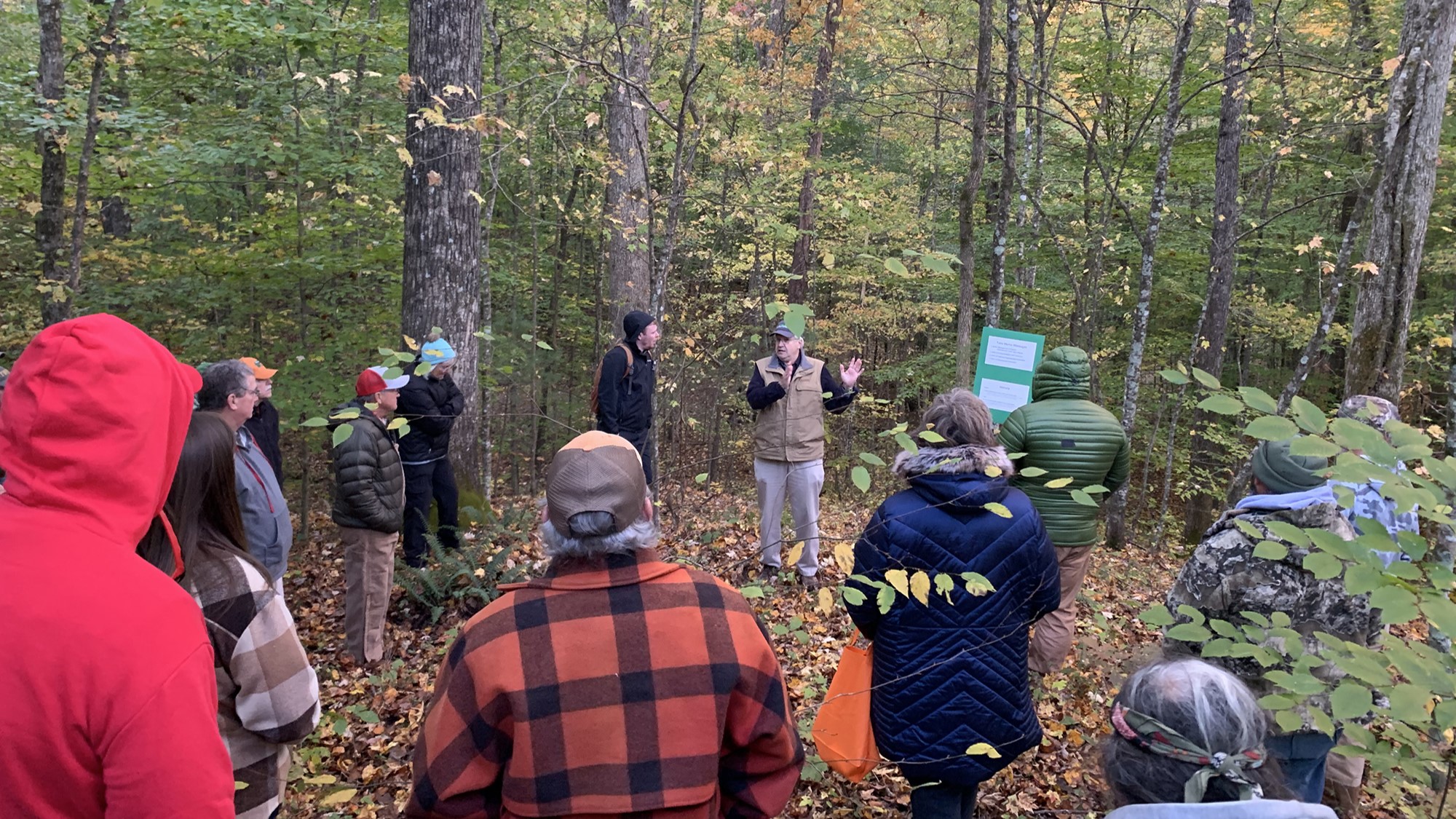 Circle of people in the woods looking at person giving a presentation