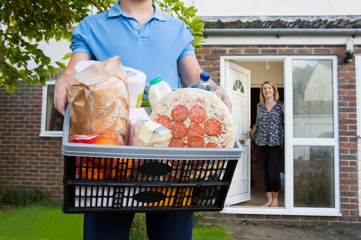 person holding a basket of groceries stands outside a house where a person opens the door