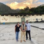 María Franco Escobar, Edwin Villa, and Carlos Trejo-Pech stand in front of a sunset and a wall that has a mural reading "La Florida"