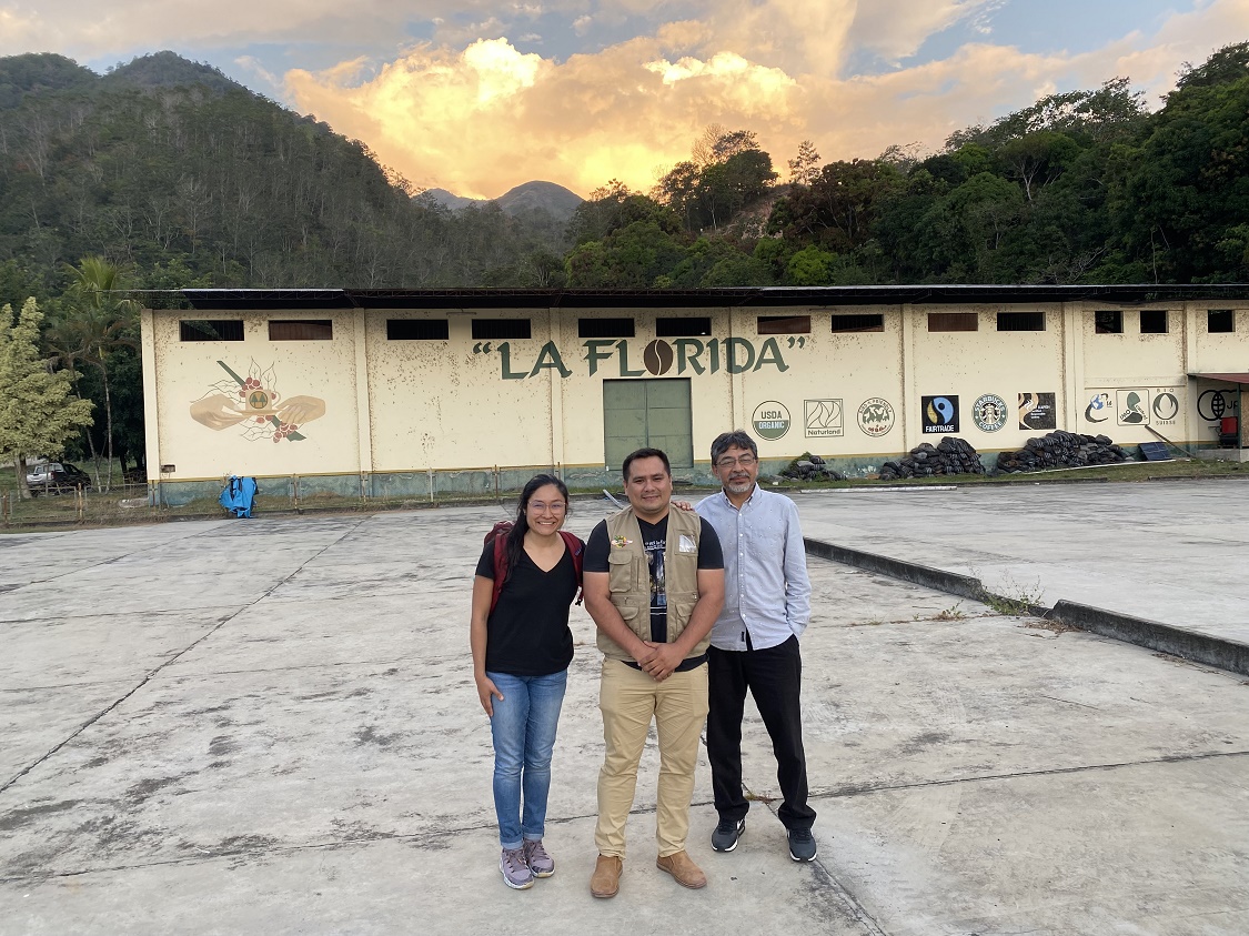 María Franco Escobar, Edwin Villa, and Carlos Trejo-Pech stand in front of a sunset and a wall that has a mural reading 