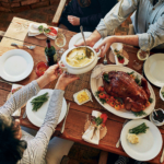 a table full of various thanksgiving foods with people's arms reaching across to serve food