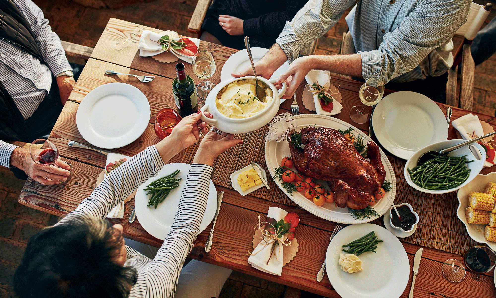 a table full of various thanksgiving foods with people's arms reaching across to serve food