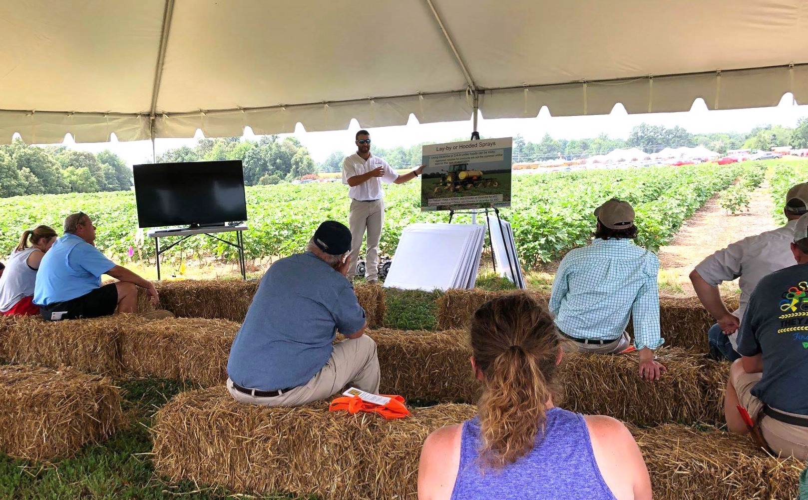 People sit on hay bales while listening to a presentation at Milan No-Till Field Day.