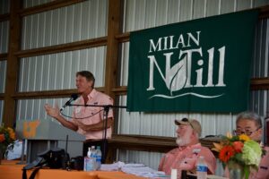 A speaker stands at a podium during Milan No-Till Field Day, a green banner that says 