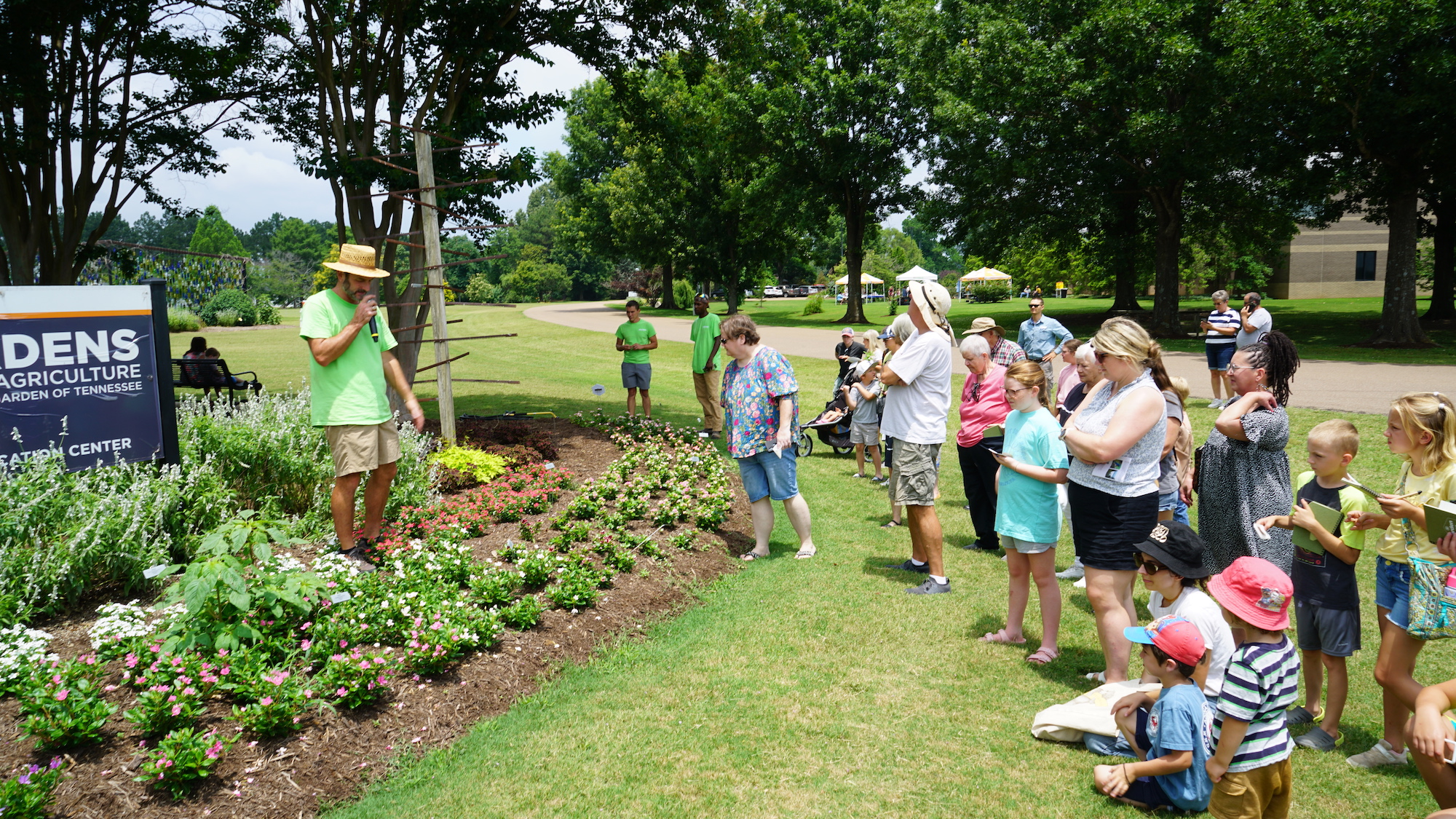 A small crowd stands in front of a flower bed during a guided tour of UT Gardens, Jackson, as a horticulturist speaks into a microphone