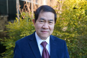 A man in a suit poses in front of a yellow bush outside