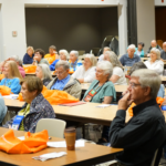 People in a crowded auditorium listen to a speaker at Fall in the Gardens