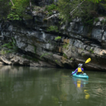 a kayaker on a river by a rock wall