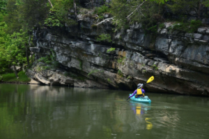 a kayaker on a river by a rock wall