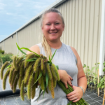 A woman holding freshly cut millet stands in a garden