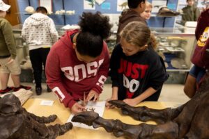 Two students examine a modern turkey’s foot and the bone structure of a Tyrannosaurus rex in the fossils classroom at the Clyde Austin 4-H Center