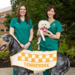 Drs. Angela Rollins (holding a small white dog) and Maryanne Murphy at a statue of UT’s famous canine mascot Smokey.