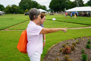 Two women point at plants at UT Gardens, Jackson, with white Summer Celebration tents in the background