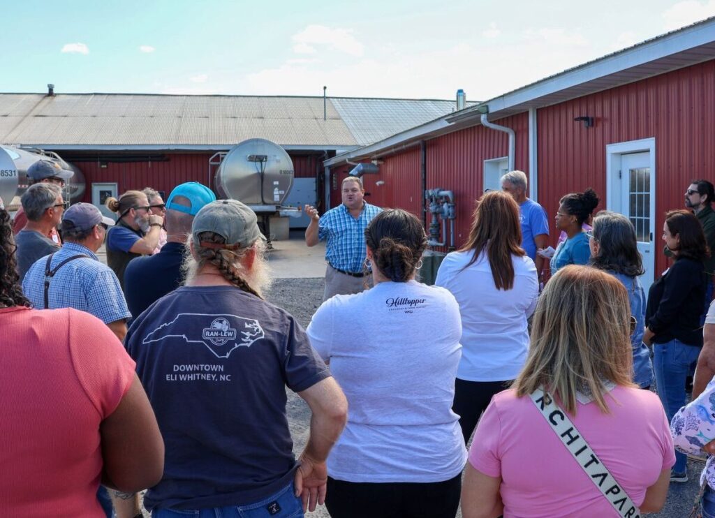 a group of people listening to a presentation outside of a dairy barn