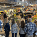 A group of adults listening to a presentation in a Whole Foods produce section