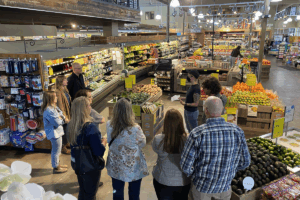 A group of adults listening to a presentation in a Whole Foods produce section