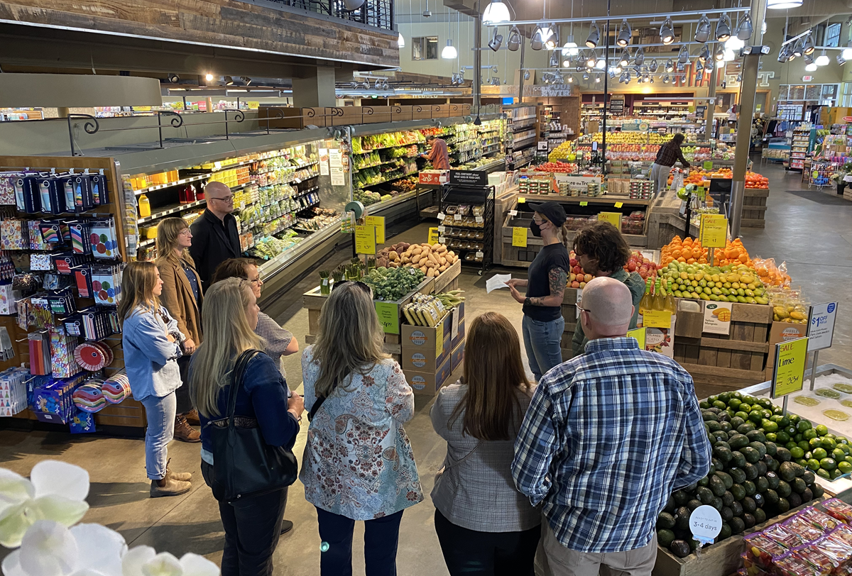 A group of adults listening to a presentation in a Whole Foods produce section