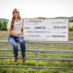 Laurel Cox sitting on a fence holding a giant check for the Durango Boots scholarship