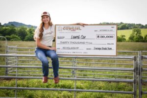 Laurel Cox sitting on a fence holding a giant check for the Durango Boots scholarship