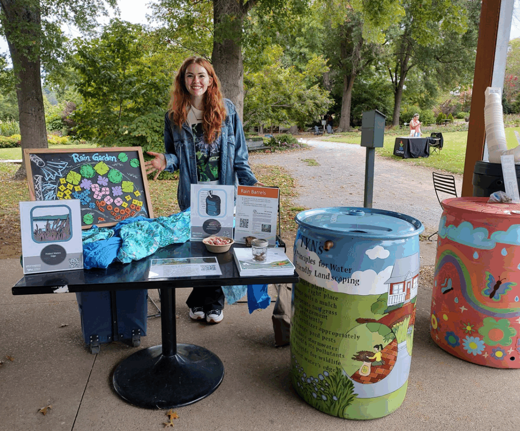 A girl posing behind a rain barrel demonstration