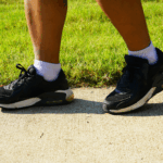 A close up of a person's black and white shoes as they walk on a concrete path next to a green lawn