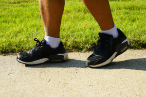 A close up of a person's black and white shoes as they walk on a concrete path next to a green lawn