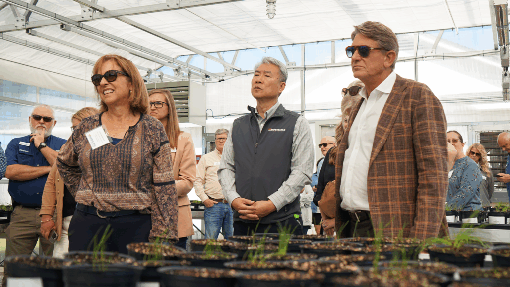 A group of people stand in a greenhouse while listening to a tour guide