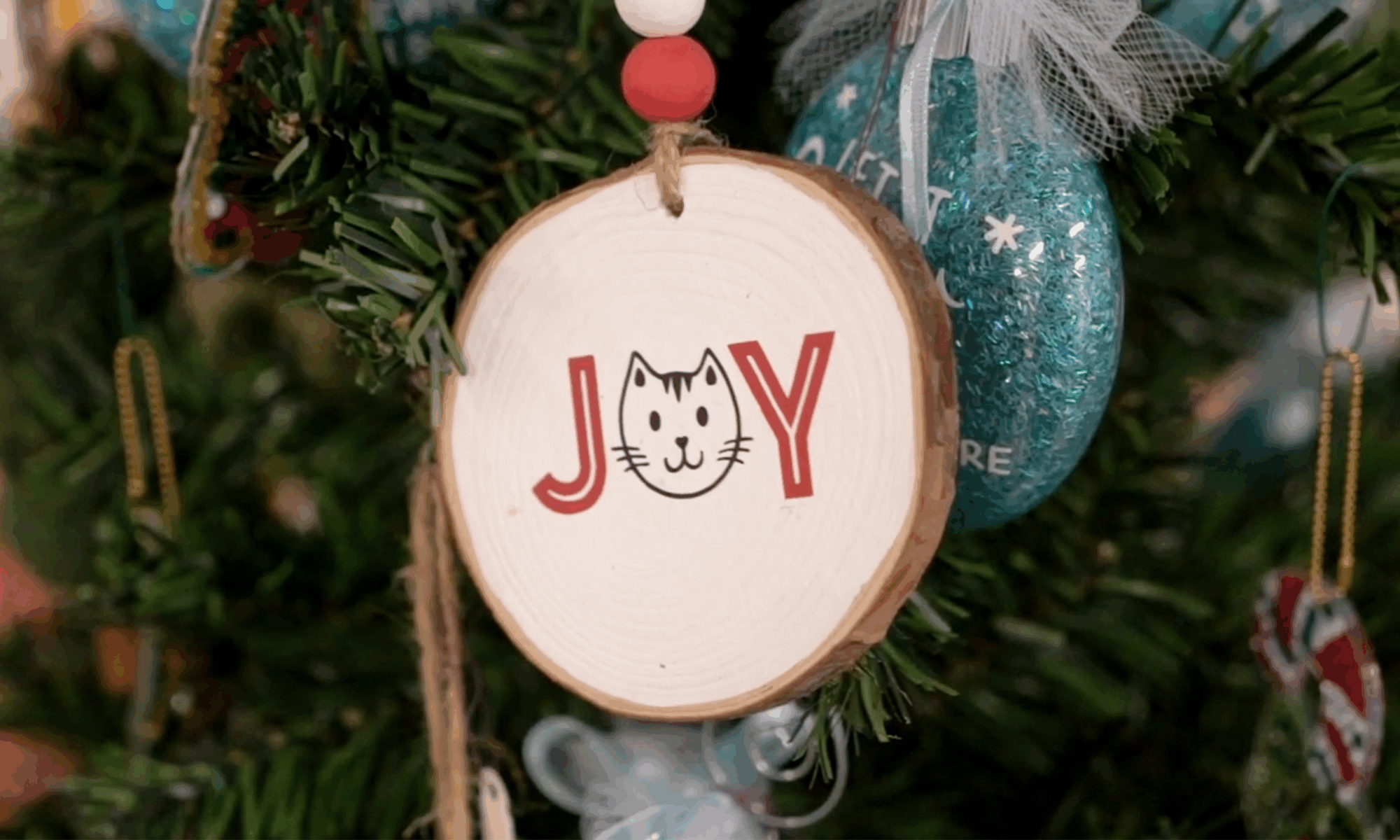 A round wooden Christmas ornament with the word "joy" painted in red letters