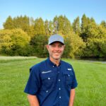 Dereck Corbin standing in a field wearing a blue shirt and a gray hat.