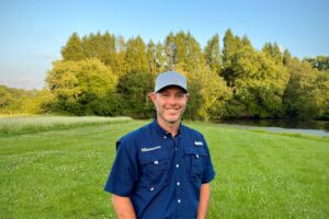 Dereck Corbin standing in a field wearing a blue shirt and a gray hat.
