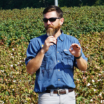 A man with a microphone speaks in front of a cotton field