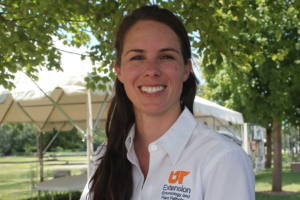 Heather Kelly smiles at the camera while wearing a white collared shirt with an orange 