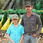 Scott Farmer and his son standing in front of farm machinery,