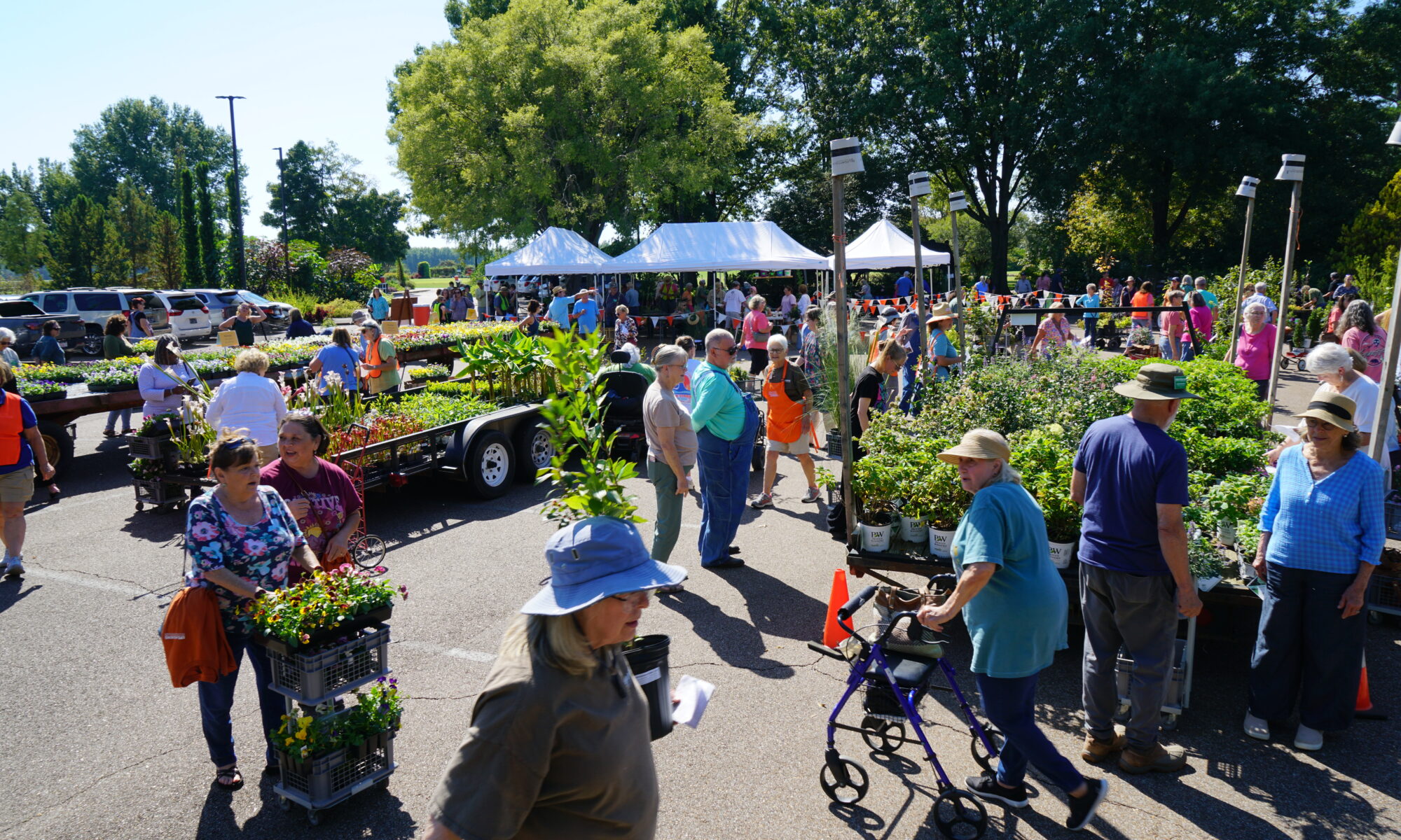 A crowd of shoppers browse trailers of plants at a plant sale