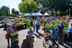 A crowd of shoppers browse trailers of plants at a plant sale