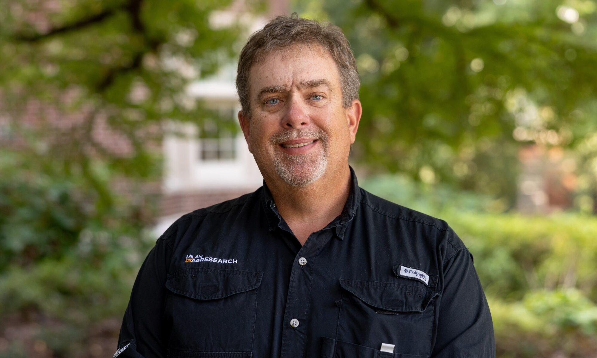 A man in a black button shirt smiles while posing for a photo