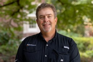 A man in a black button shirt smiles while posing for a photo
