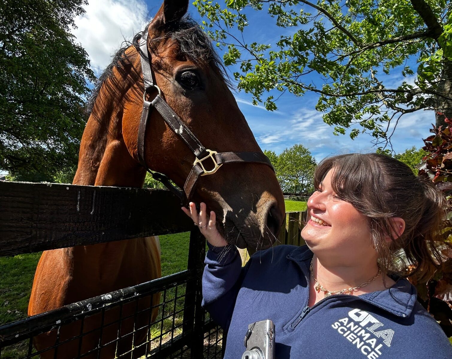A woman stands smiling at a horse.