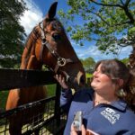 A woman stands smiling at a horse.